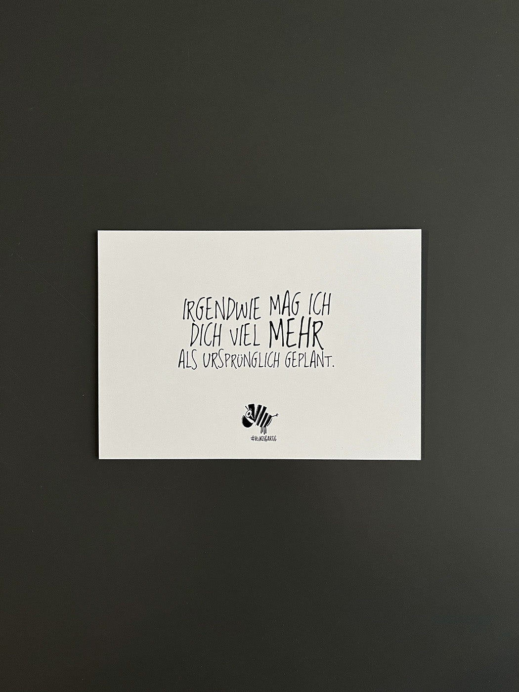 Weiße Postkarte von #heinzigartig mit dem Spruch: "Irgendwie mag ich dich viel mehr, als ursprünglich geplant"