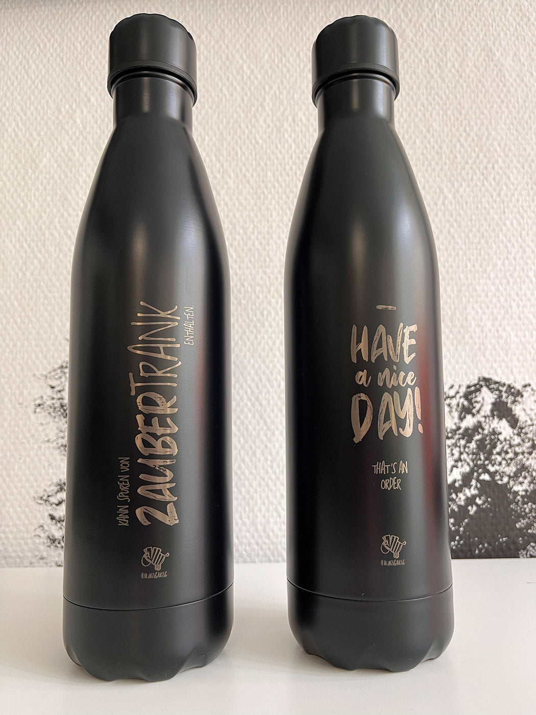 Zwei Schwarze Isolierflaschen aus der #heinzigartig-Kollektion mit Sprüchen