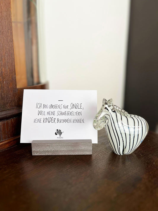 Weiße Postkarte von #heinzigartig mit dem Spruch: "Ich bin übrigens nur Single, weil meine Schwiegereltern keine Kinder bekommen können."