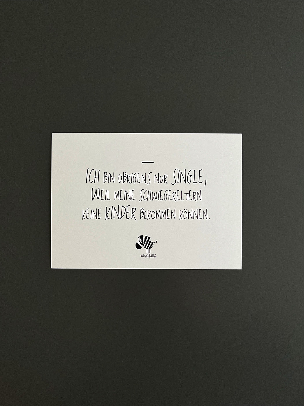 Weiße Postkarte von #heinzigartig mit dem Spruch: "Ich bin übrigens nur Single, weil meine Schwiegereltern keine Kinder bekommen können."