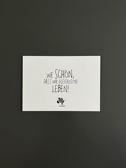 Weiße Postkarte von #heinzigartig mit dem Spruch: "Wie schön, dass wir gleichzeitig leben!"