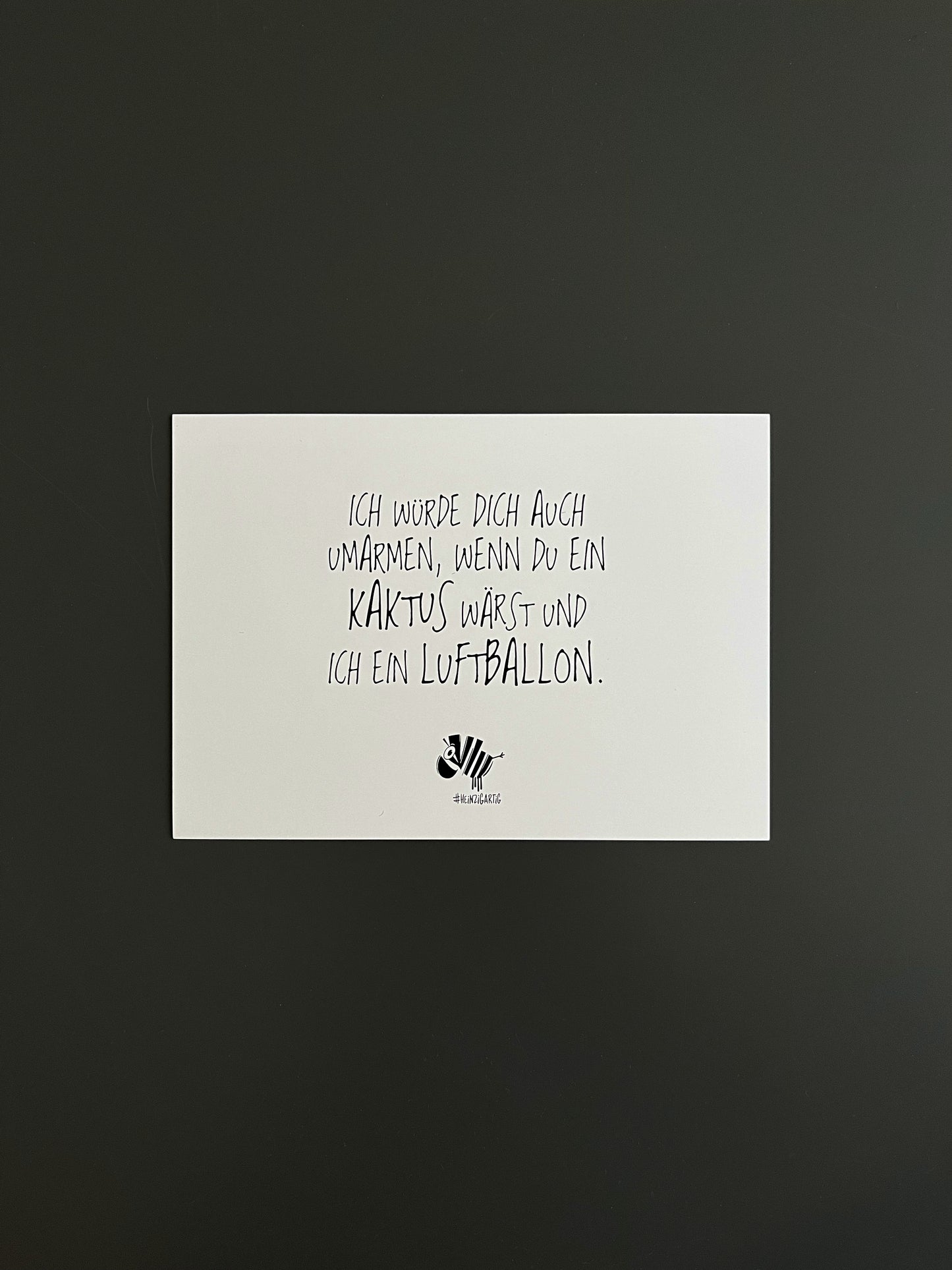Weiße Postkarte von #heinzigartig mit dem Spruch: "Ich würde dich auch umarmen, wenn du ein Kaktus wärst und ich ein Luftballon."